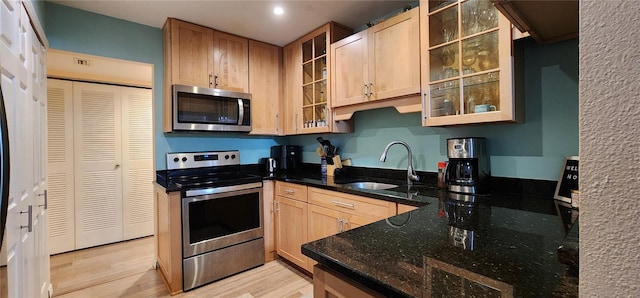 kitchen with a sink, light brown cabinets, light wood-style flooring, dark stone counters, and stainless steel appliances