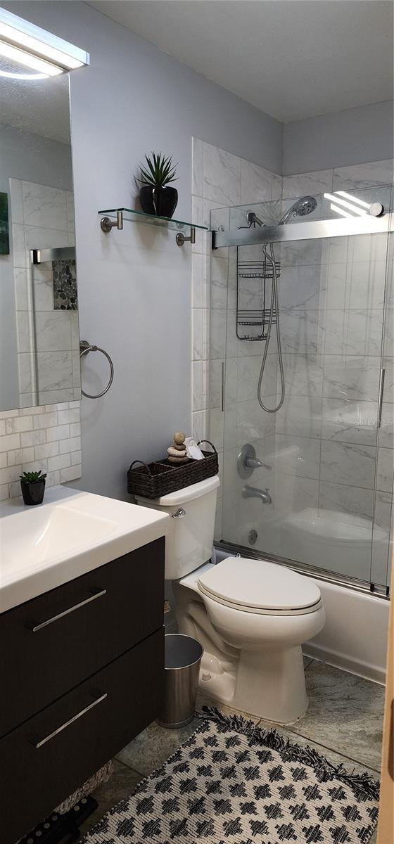 full bath featuring vanity, tile patterned flooring, combined bath / shower with glass door, and toilet