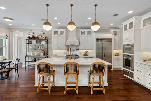 kitchen featuring visible vents, appliances with stainless steel finishes, light countertops, premium range hood, and a warming drawer