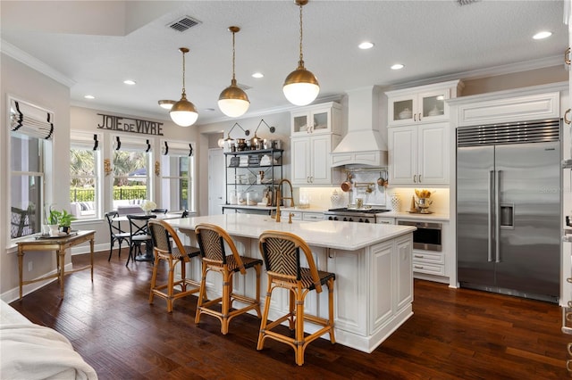 kitchen with visible vents, crown molding, premium range hood, backsplash, and stainless steel built in refrigerator