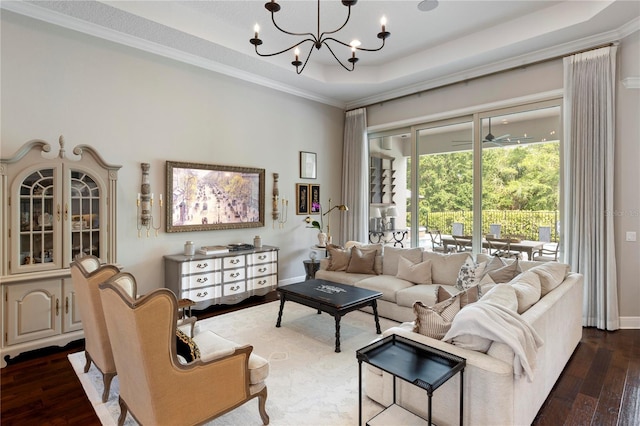 living room with dark wood-type flooring, a raised ceiling, crown molding, and a chandelier