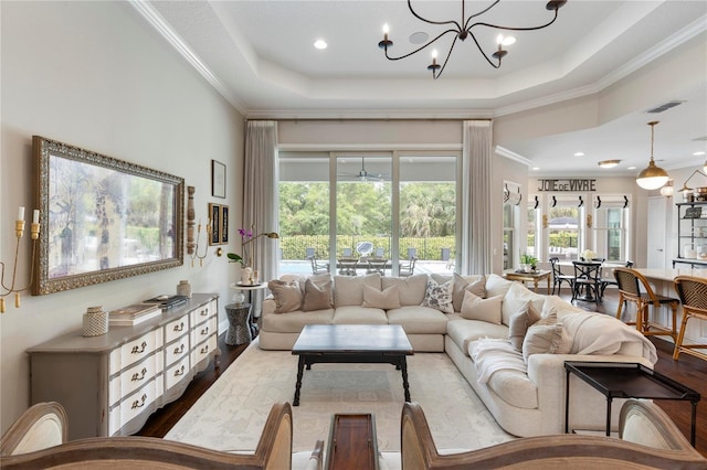 living area featuring a chandelier, dark wood finished floors, a tray ceiling, visible vents, and ornamental molding