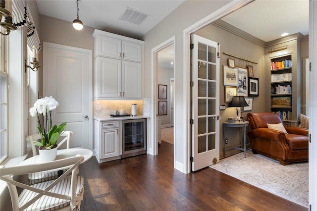 sitting room with crown molding, dark wood-style flooring, beverage cooler, visible vents, and a bar