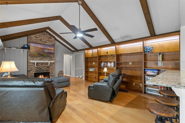 living area with a ceiling fan, visible vents, a brick fireplace, vaulted ceiling with beams, and light wood-style flooring