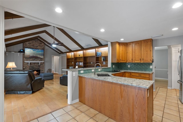 kitchen featuring light stone counters, a sink, freestanding refrigerator, a peninsula, and open floor plan