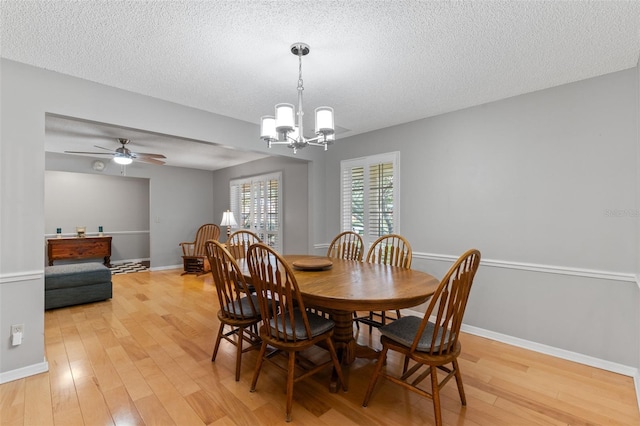 dining space with baseboards, ceiling fan with notable chandelier, light wood finished floors, and a textured ceiling