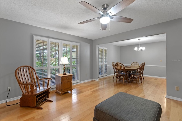 dining space with a textured ceiling, baseboards, light wood-style flooring, and ceiling fan with notable chandelier