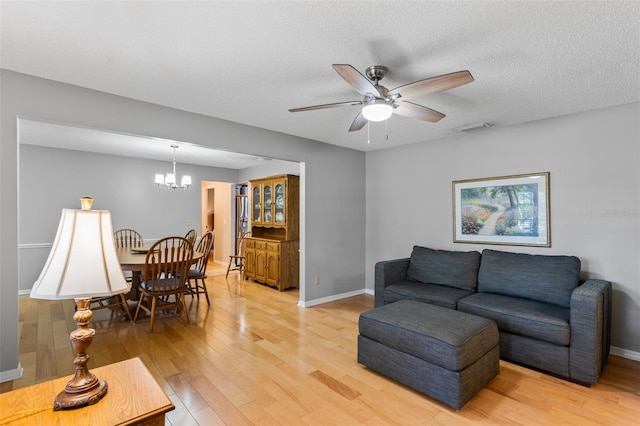 living room with visible vents, light wood finished floors, and ceiling fan with notable chandelier