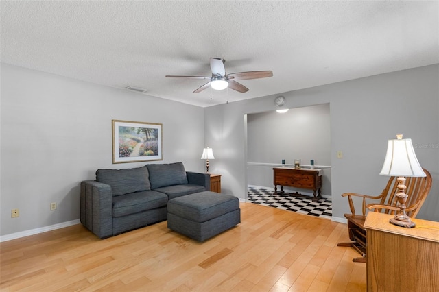 living area featuring light wood finished floors, a textured ceiling, a ceiling fan, baseboards, and visible vents