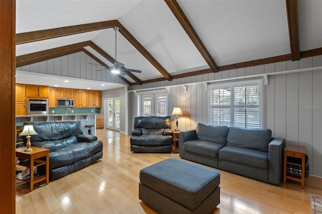 living area with beam ceiling, light wood-style floors, high vaulted ceiling, a textured ceiling, and a ceiling fan