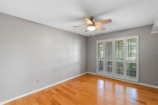 empty room with a ceiling fan, baseboards, light wood finished floors, and a textured ceiling