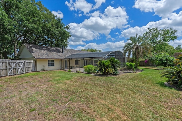 rear view of house with a lawn, a fenced backyard, a lanai, and stucco siding