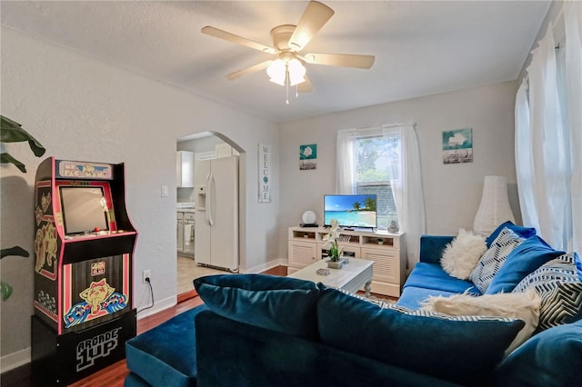 living room featuring arched walkways, baseboards, a ceiling fan, and wood finished floors