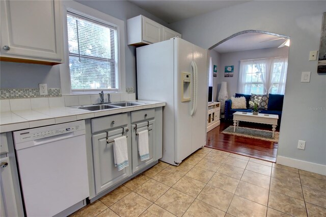 kitchen featuring arched walkways, a sink, white cabinets, tile counters, and white appliances