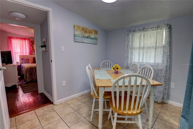 dining area with light tile patterned floors, baseboards, a textured ceiling, and lofted ceiling