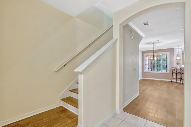 stairs featuring visible vents, arched walkways, wood finished floors, baseboards, and a notable chandelier