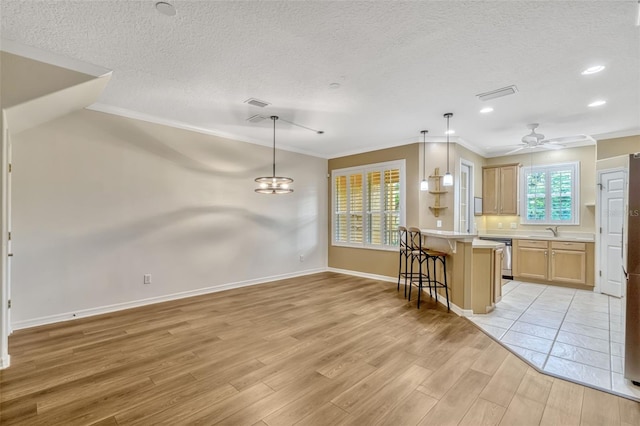 kitchen featuring crown molding, visible vents, a kitchen bar, light wood-type flooring, and a sink