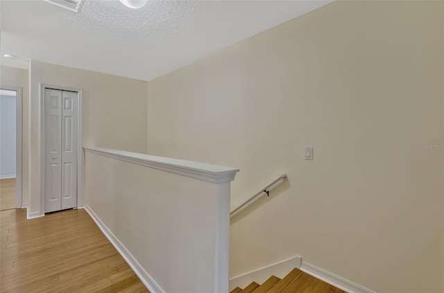 stairway with a textured ceiling, baseboards, visible vents, and wood finished floors