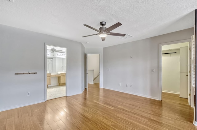 unfurnished bedroom featuring visible vents, a textured ceiling, light wood-style flooring, baseboards, and a spacious closet