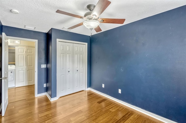 unfurnished bedroom featuring a textured ceiling, washer / clothes dryer, baseboards, wood finished floors, and a closet