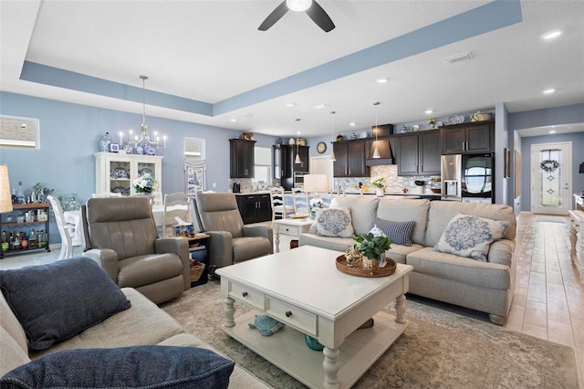 living area with a raised ceiling, ceiling fan with notable chandelier, recessed lighting, baseboards, and visible vents