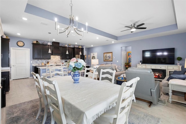 dining room featuring light wood-style floors, recessed lighting, a raised ceiling, and ceiling fan with notable chandelier