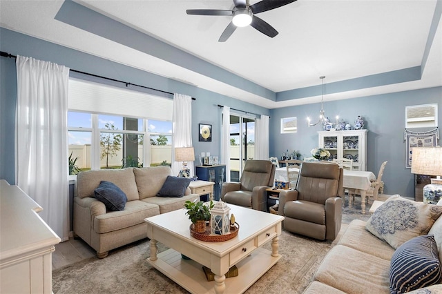 living room featuring a tray ceiling and ceiling fan with notable chandelier