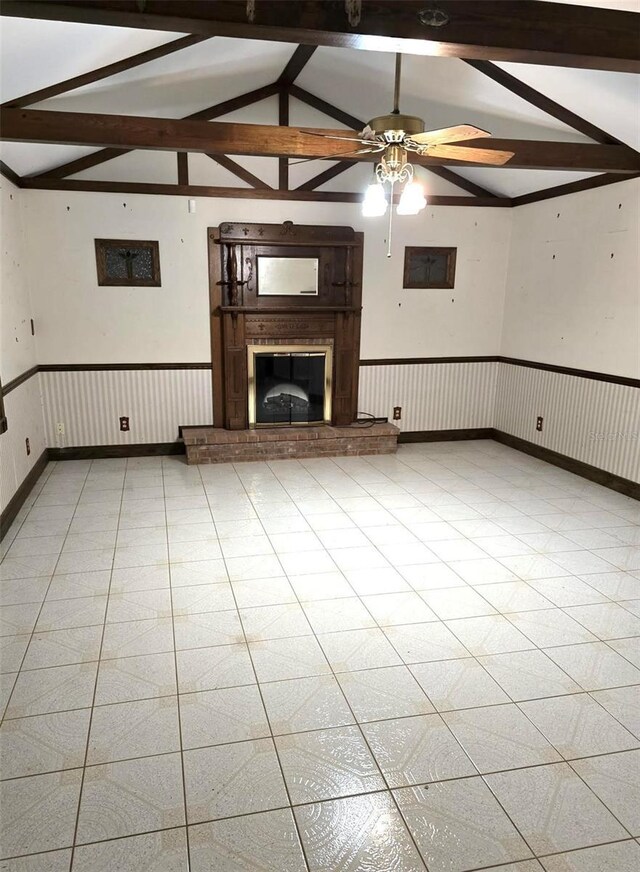 unfurnished living room featuring a fireplace, a ceiling fan, vaulted ceiling with beams, and a wainscoted wall