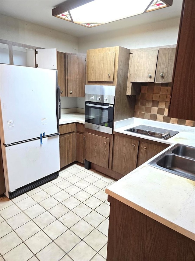 kitchen with freestanding refrigerator, oven, black electric stovetop, light countertops, and a sink