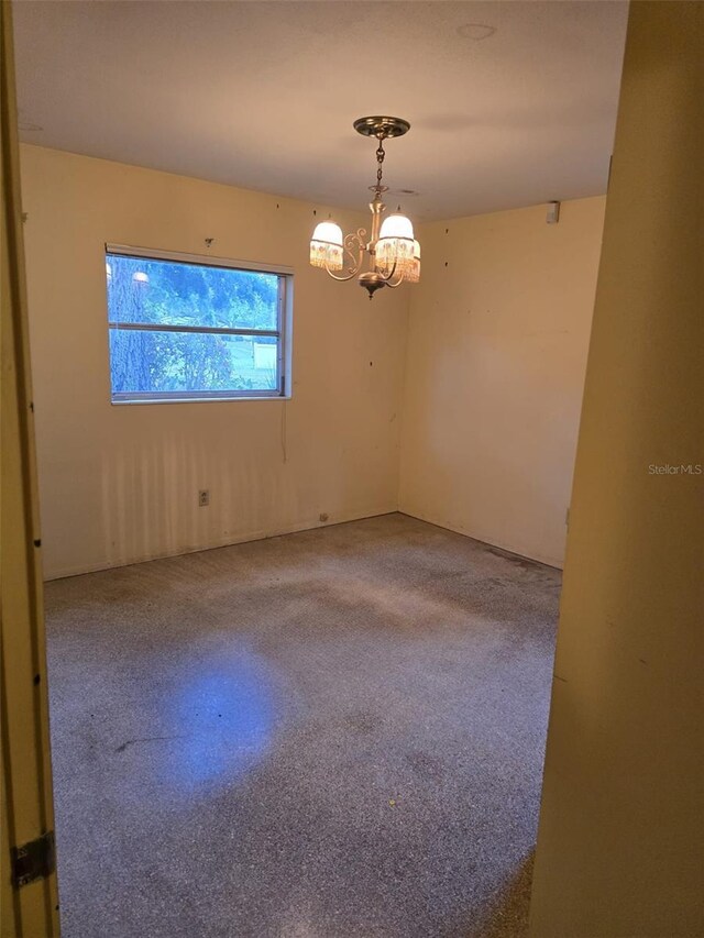 carpeted spare room featuring a chandelier