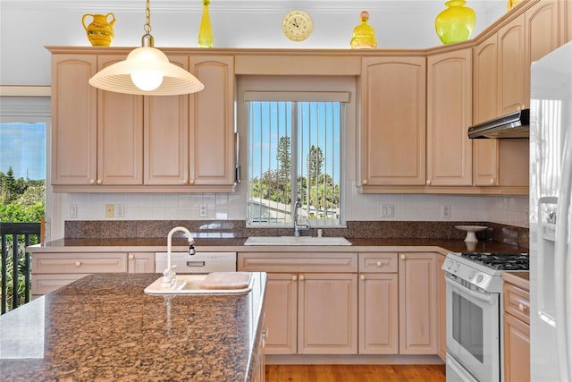 kitchen with backsplash, light brown cabinetry, a sink, under cabinet range hood, and white appliances