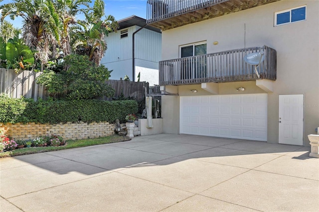 exterior space featuring fence, stucco siding, concrete driveway, and a balcony