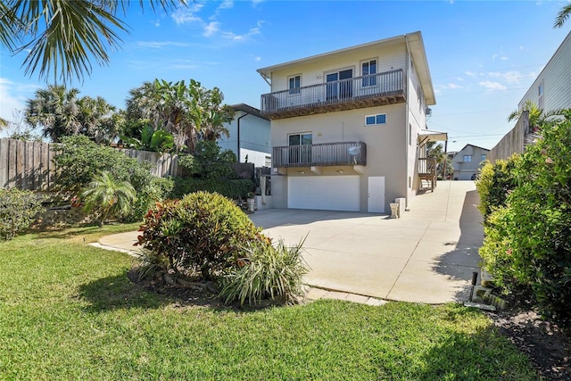 rear view of property with fence, stucco siding, concrete driveway, a balcony, and a yard