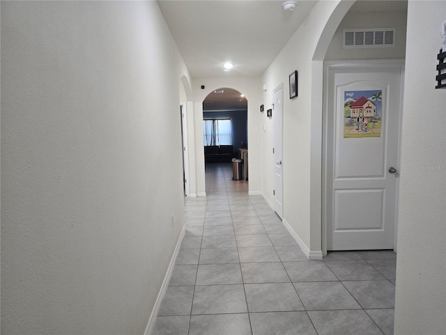 hall featuring arched walkways, baseboards, visible vents, and light tile patterned floors