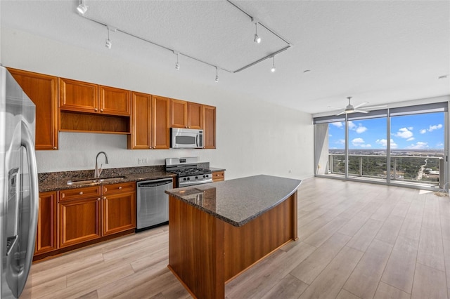 kitchen with brown cabinets, a sink, dark stone countertops, stainless steel appliances, and light wood-type flooring