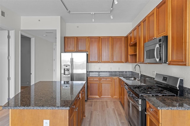 kitchen with a kitchen island, dark stone countertops, a sink, light wood-style flooring, and stainless steel appliances