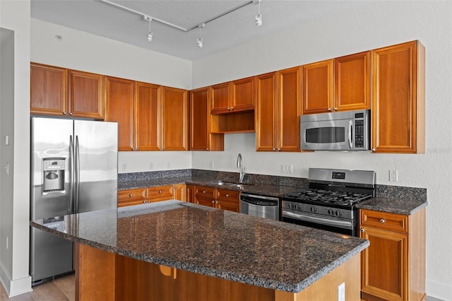 kitchen with a center island, a sink, track lighting, dark stone counters, and stainless steel appliances