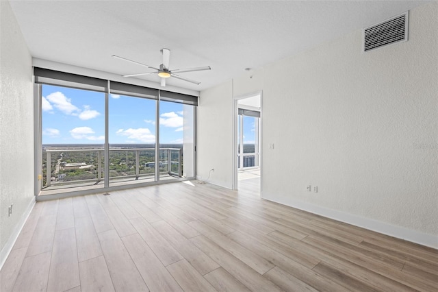 spare room with a textured wall, a ceiling fan, wood finished floors, and visible vents