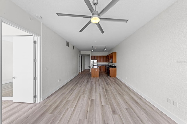 unfurnished living room featuring light wood-style floors, baseboards, ceiling fan, and attic access
