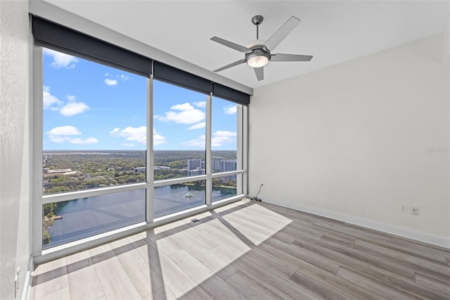 spare room featuring a ceiling fan, baseboards, floor to ceiling windows, and wood finished floors