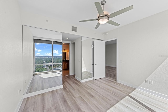 spare room with visible vents, a wall of windows, light wood-style floors, baseboards, and ceiling fan