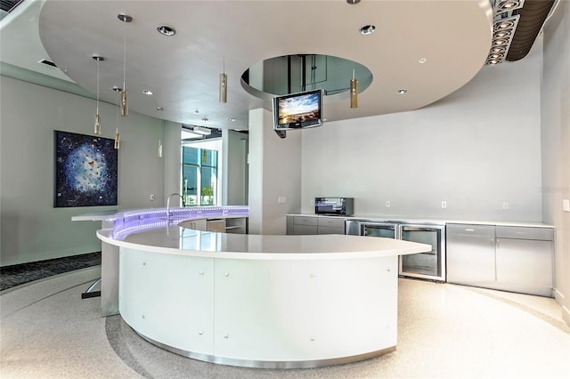 kitchen with a sink, light countertops, beverage cooler, light speckled floor, and a large island with sink