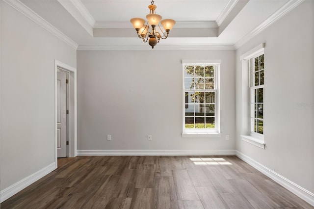 unfurnished room featuring a raised ceiling, ornamental molding, wood finished floors, and a notable chandelier