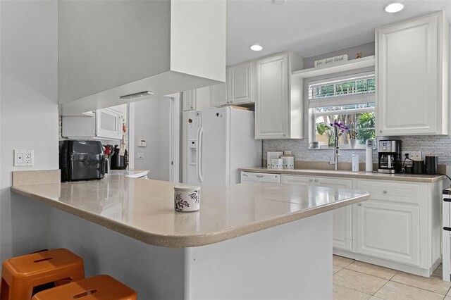 11908 Delfina Ln, Orlando, FL 32827 - kitchen with light tile patterned floors, a kitchen breakfast bar, white cabinets, white refrigerator with ice dispenser, and backsplash