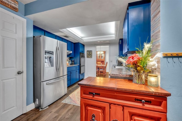 kitchen with blue cabinetry, visible vents, wood finished floors, a raised ceiling, and stainless steel fridge