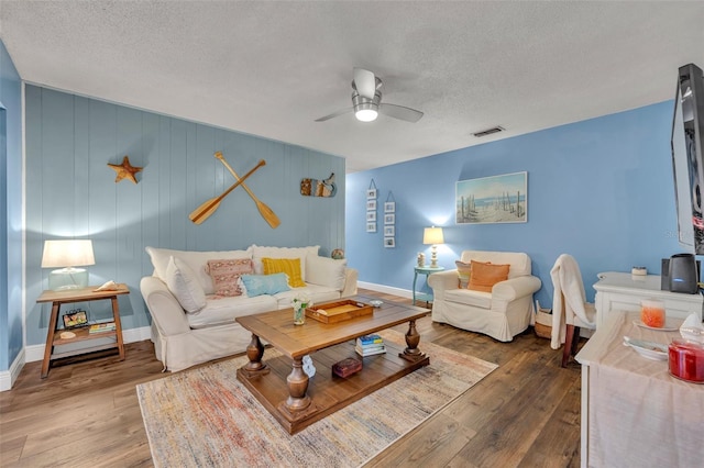 living area with a textured ceiling, a ceiling fan, wood finished floors, and visible vents