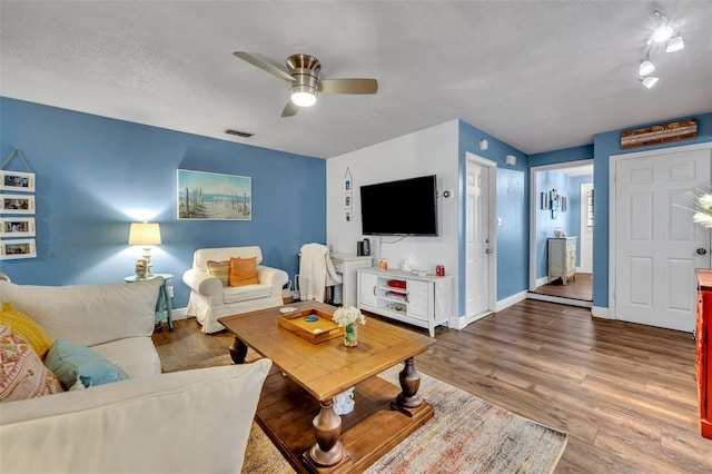 living room featuring baseboards, a ceiling fan, wood finished floors, and visible vents