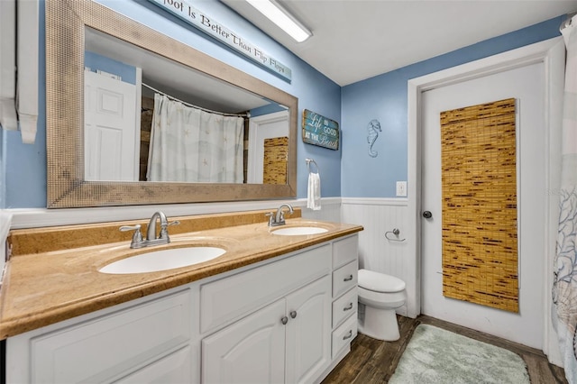 full bath with a sink, wainscoting, toilet, and wood finished floors