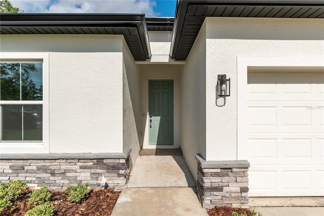 view of exterior entry featuring a garage, stucco siding, and stone siding