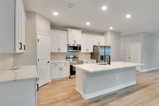 kitchen with decorative backsplash, visible vents, a center island with sink, light wood-style floors, and stainless steel appliances